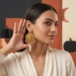 Elegant woman wearing One Gram Gold Lord Ganesha Temple Earrings with pearl tassels, ruby and emerald stone accents, and traditional gold-plated design.
